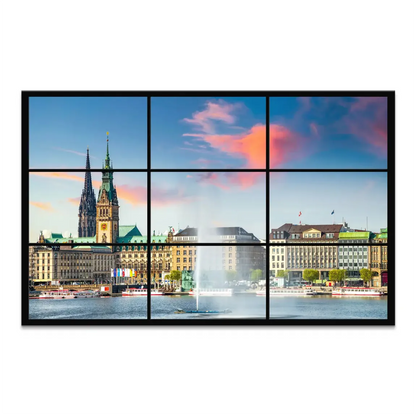 Panoramic Hamburg sunset viewed through a modern multi-pane window, highlighting Rathaus and church spires with the Inner Alster fountain.