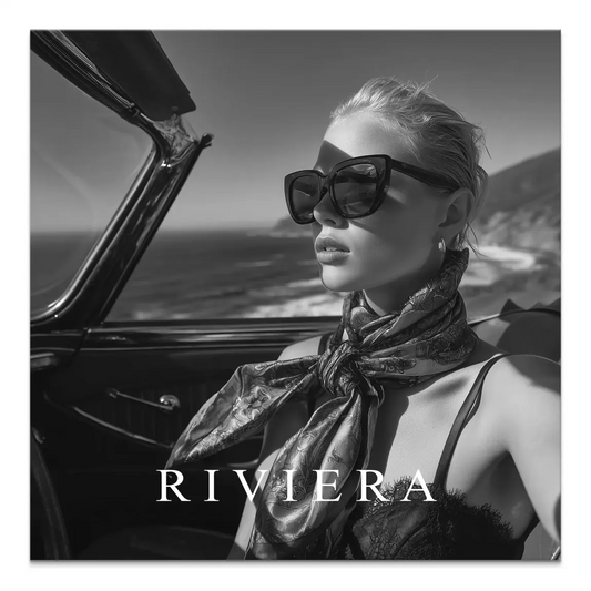 Black-and-white photo of a glamorous woman with windswept hair, sunglasses, and a silk scarf driving a vintage convertible along a coastal road.