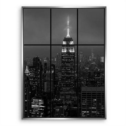 Empire State Building focal point in nocturnal New York captured in grayscale with window-frame perspective.
